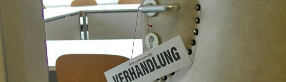 Blick auf ein Sitzungszimmer durch eine halbgeöffnete Tür. An der Türklinke hängt ein Schild 'Verhandlung'. (Foto: UVS)